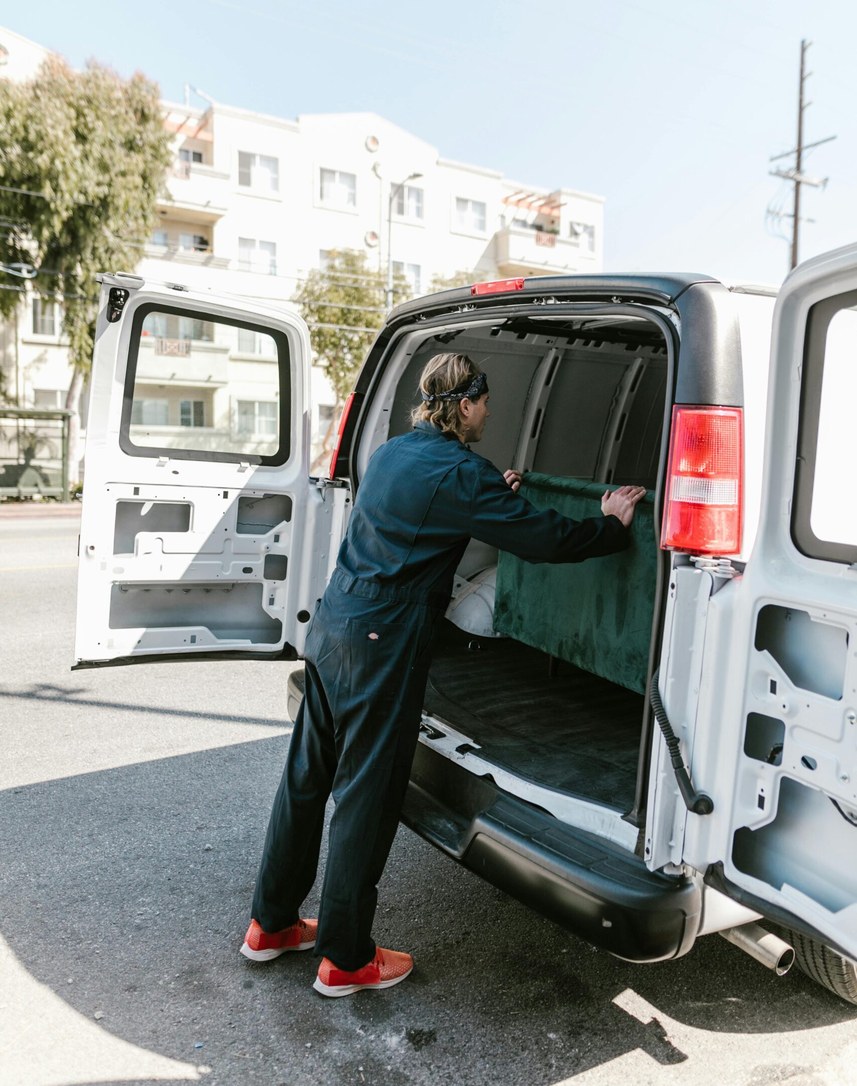 A worker in blue coveralls loads a van on a sunny day for a moving service.